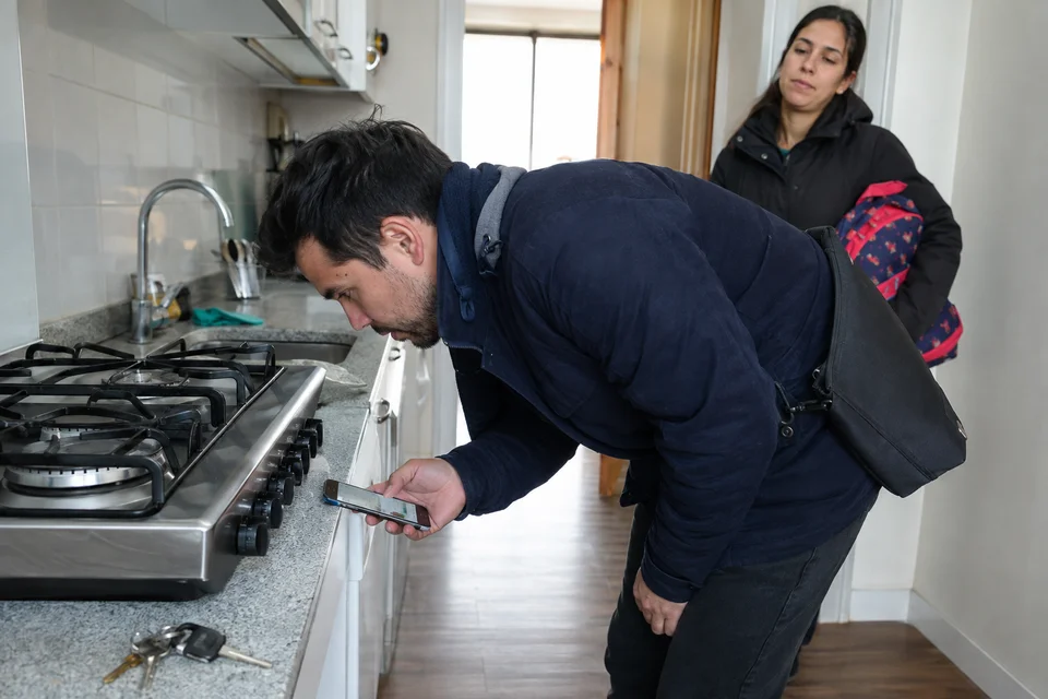 Hombre listo para salir fotografía los mandos apagados de la cocina mientras su pareja lo espera